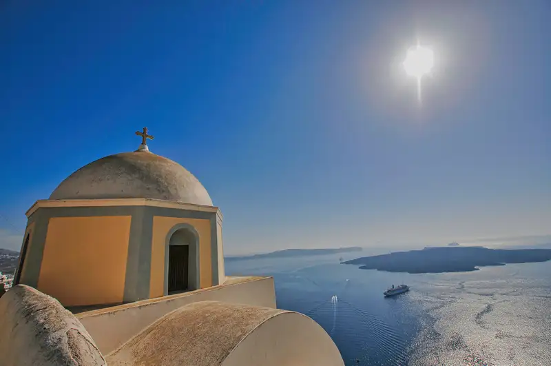 Domed church above the Santorini caldera with a cruise ship on the sea below