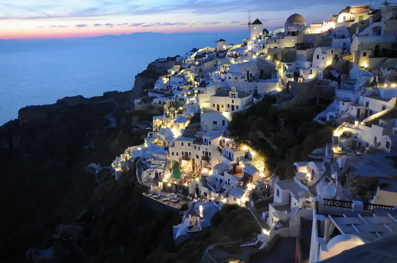 The cascading white houses of Oia in Santorini glowing after sunset