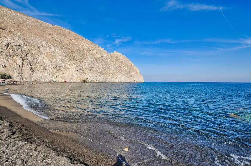 The volcanic shore of Perissa in Santorini with the headland rising at one end