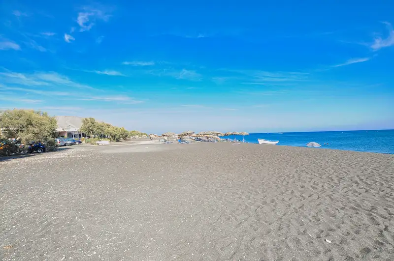 The long black sand beach of Perivolos in Santorini with umbrellas and beach bars