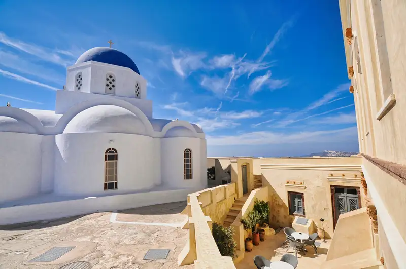 Whitewashed chapel of Pyrgos framed by a yellow wall and arched windows in Santorini
