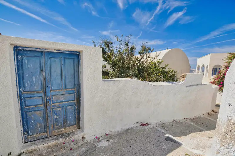 A weathered blue wooden door set in a whitewashed wall in Oia, Santorini