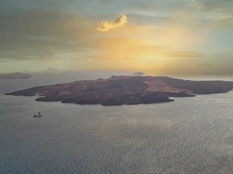 The volcanic island of Nea Kameni in the Santorini caldera at sunset with a small boat passing