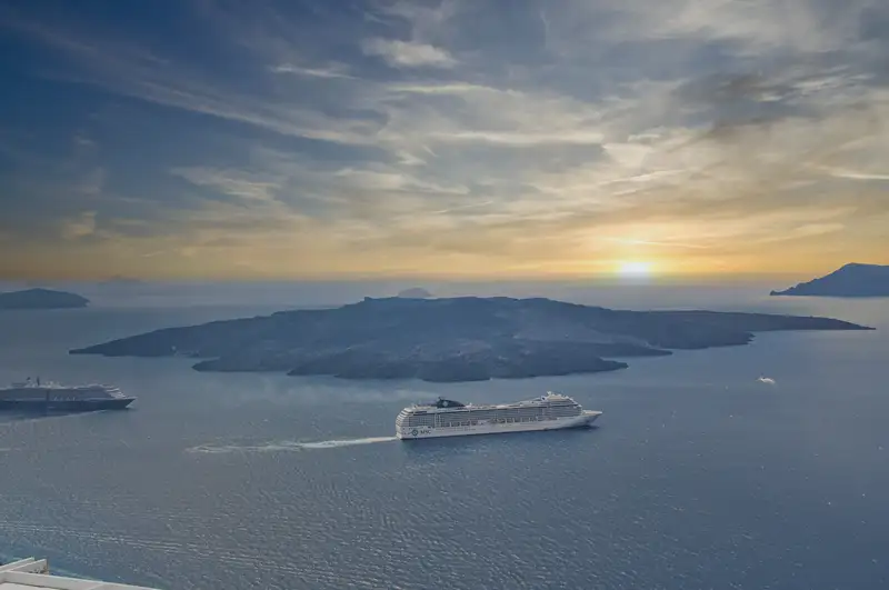A cruise ship crossing the Santorini caldera in front of the volcano at sunset