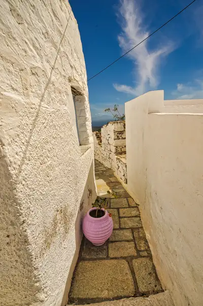 Slim stone-paved alley between white walls in the old town of Chora