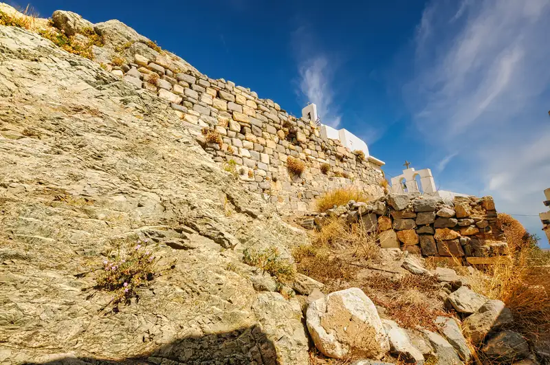 Rocky slope rising to old fortification walls and a white chapel in Chora, Serifos