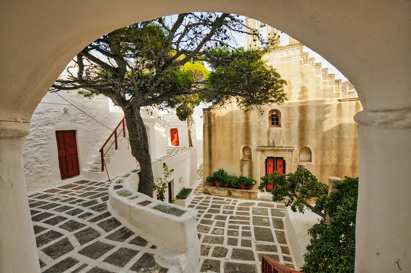 Shaded courtyard with a tree and red door inside the Monastery of Taxiarches, Serifos