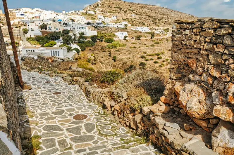 Stone path descending toward the village of Chora Sikinos with terraced hills
