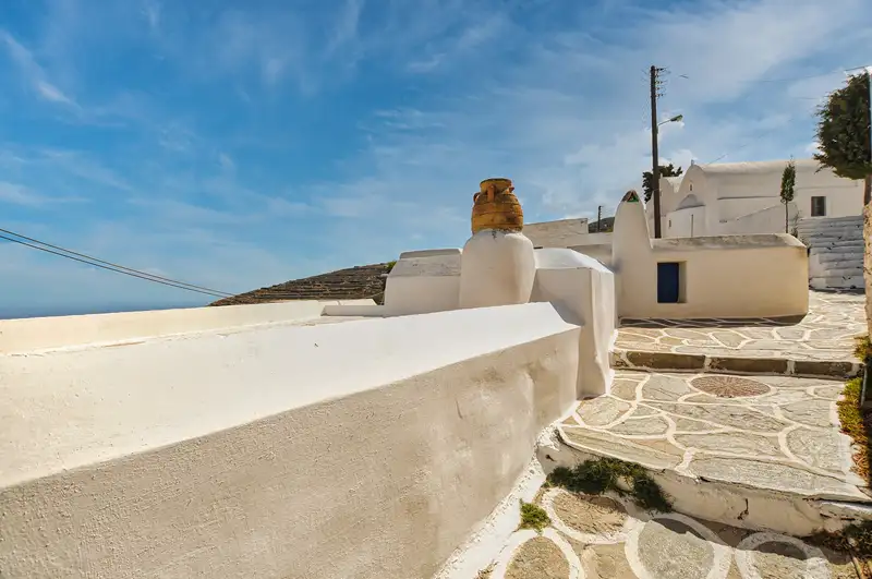 Whitewashed wall and stone path in Chorio Sikinos with an amphora and the sea beyond