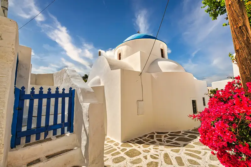 Whitewashed church with a blue dome and bougainvillea in Chora Sikinos