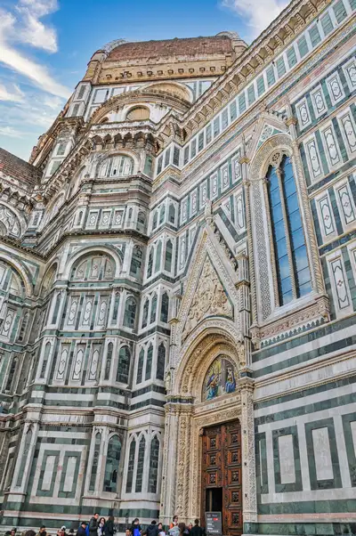 Detailed side view of the green and white marble facade of Florence Cathedral with its carved doorway