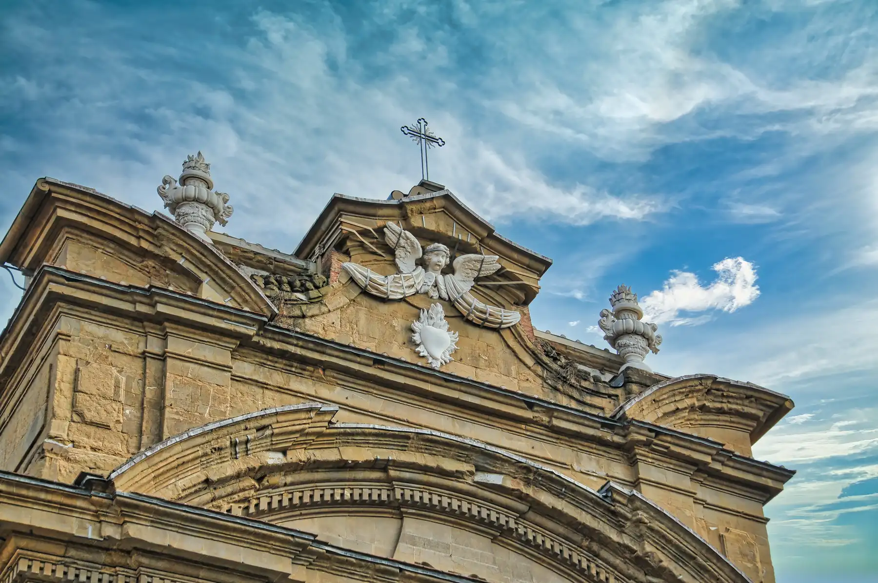 Baroque church facade in Florence topped with a stone angel, a flaming heart, and an iron cross