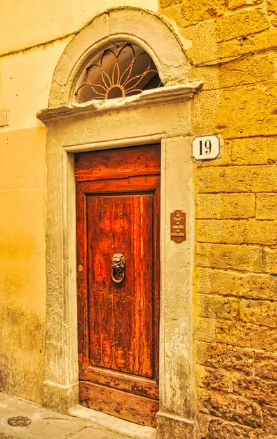 Weathered red wooden door with a lion knocker and a fan-shaped window on a Florence street