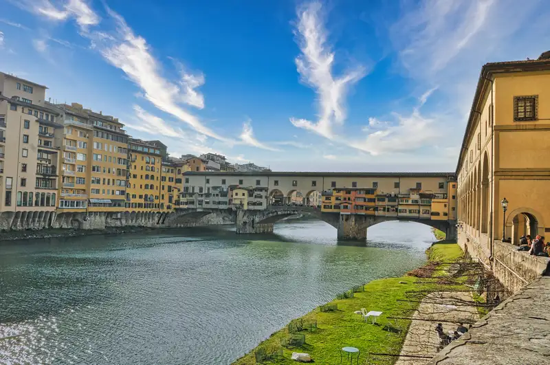 Ponte Vecchio spanning the Arno river seen from the grassy bank in Florence