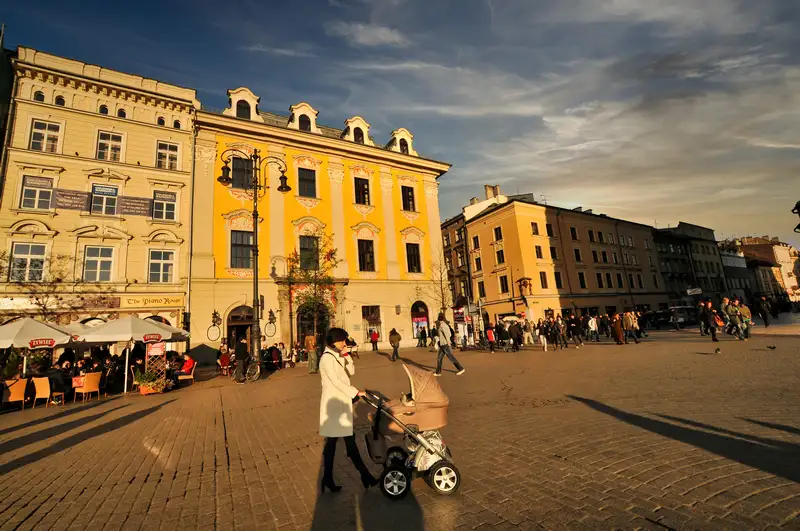 People crossing the cobbles of Krakow's Main Market Square past cafe tables