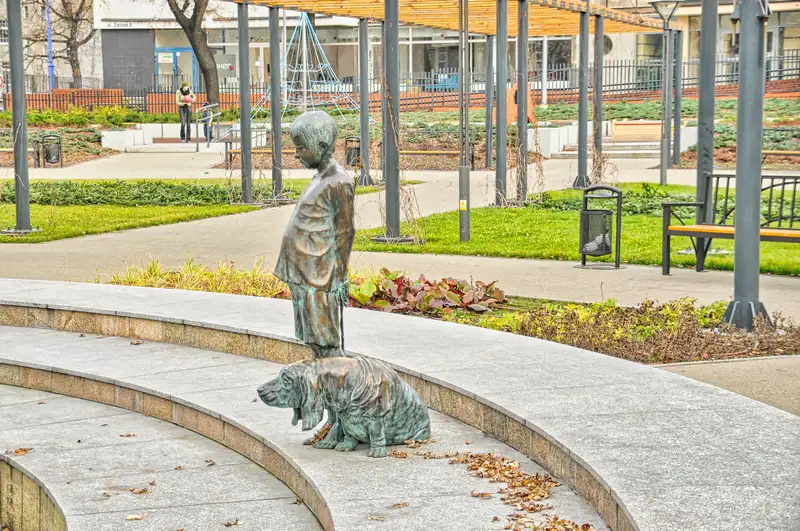 Bronze sculpture of a boy with a dog in a park in Poznan