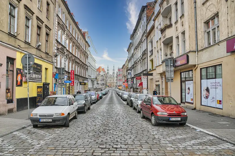 Cobbled street in Poznan lined with cars leading toward the Bernardine Church