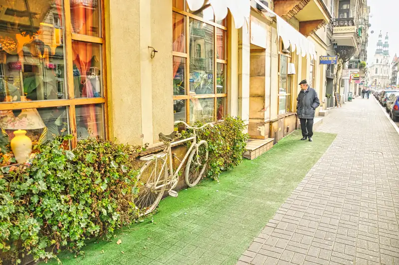 White bicycle leaning against ivy outside a shop in central Poznan